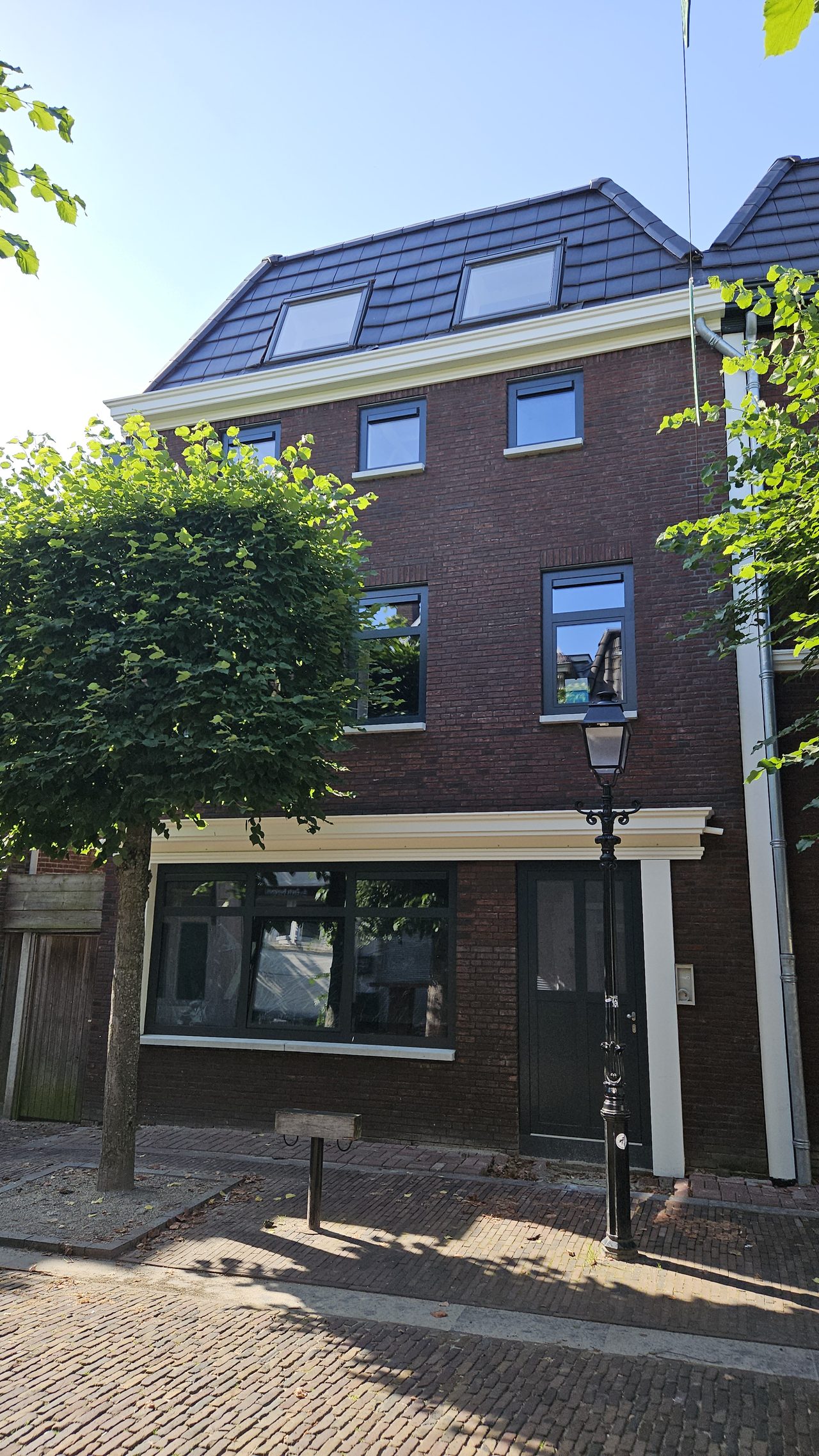Gerestaureerde straatgevel met een lantaarn ervoor en een boom naast de deur