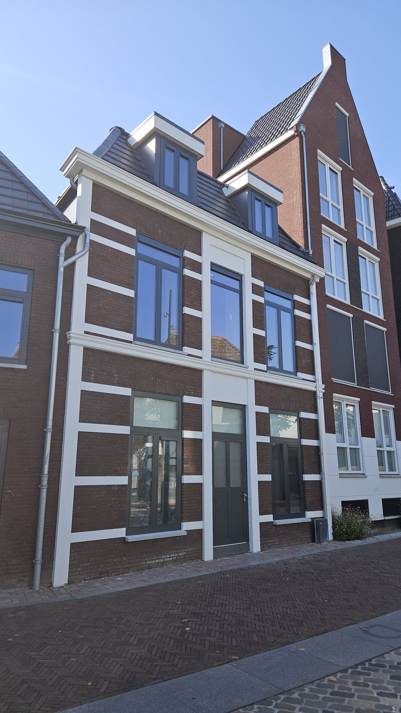 Gerestaureerde gevel met witte speklagen, naast een pand met een trapgevel