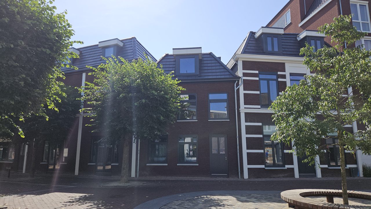 Het appartementengebouw vanaf de straat, met bomen ervoor en verspringende kappen