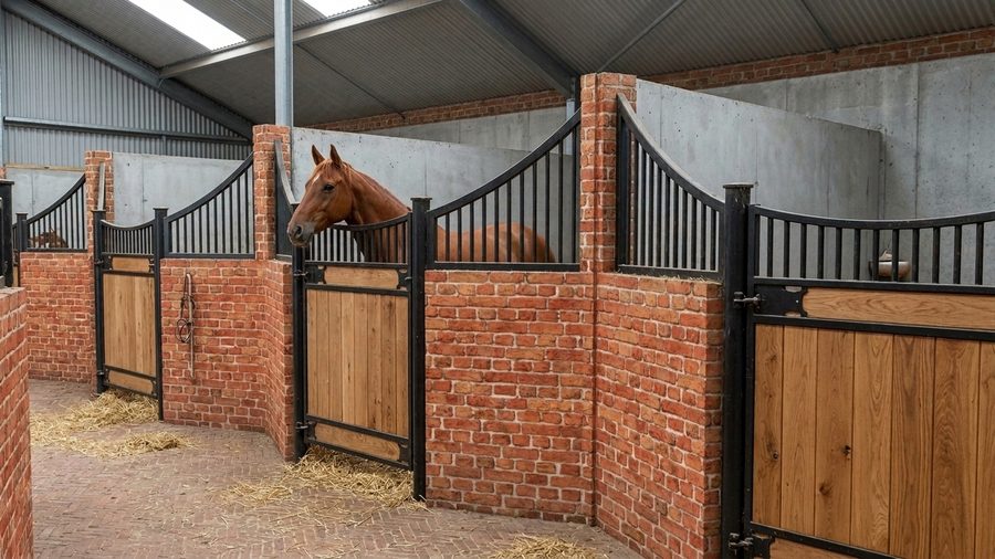 Modelbeeld van paardenboxen met zwart hekwerk tegen een gemetselde wand