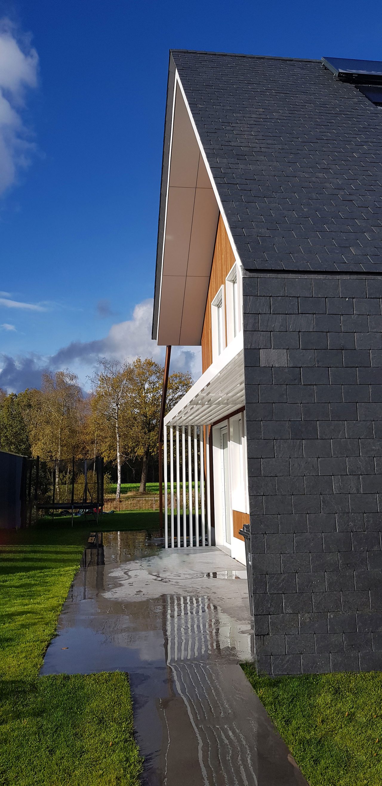 Zijgevel van de woning met een overstek boven de gevel, kort na regen