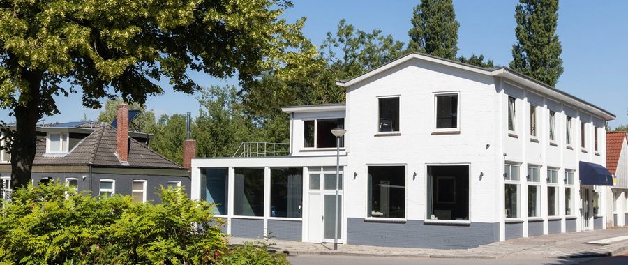 Wit geschilderd hoekpand in Bad Nieuweschans met een grijze plint en een glazen serre