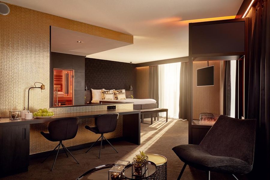 Hotelkamer in donkere tinten, met een sauna zichtbaar via de spiegelwand