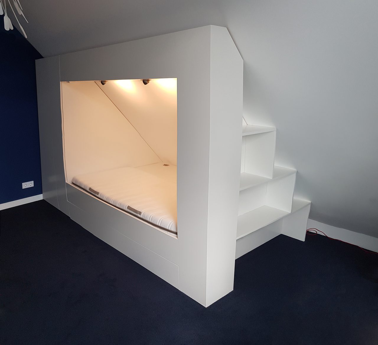 Witte ingebouwde bedstee met een verlichte slaapnis en een trap die eromheen loopt