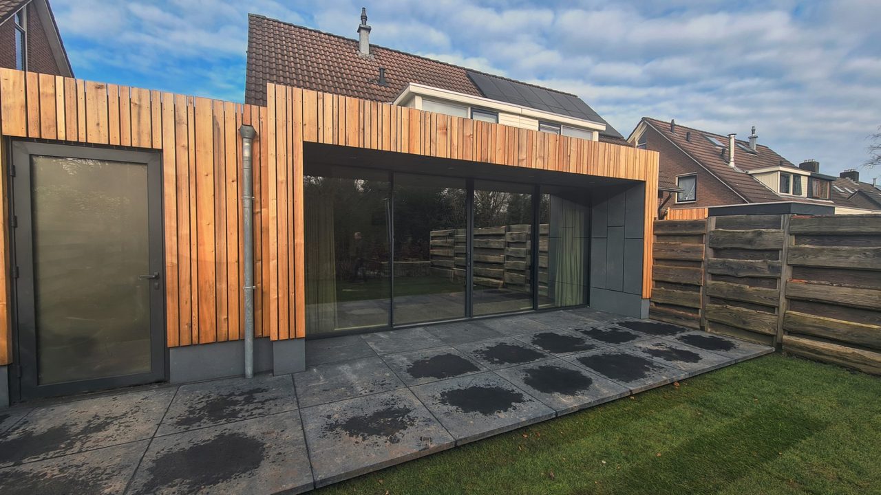 De uitbouw schuin van opzij, met de bestaande woning erachter