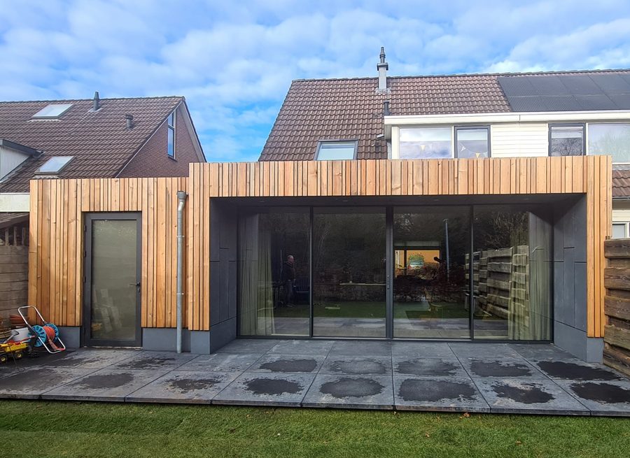 Uitbouw in Zuidlaren met een houten gevel en grote glazen schuifpuien naar het terras