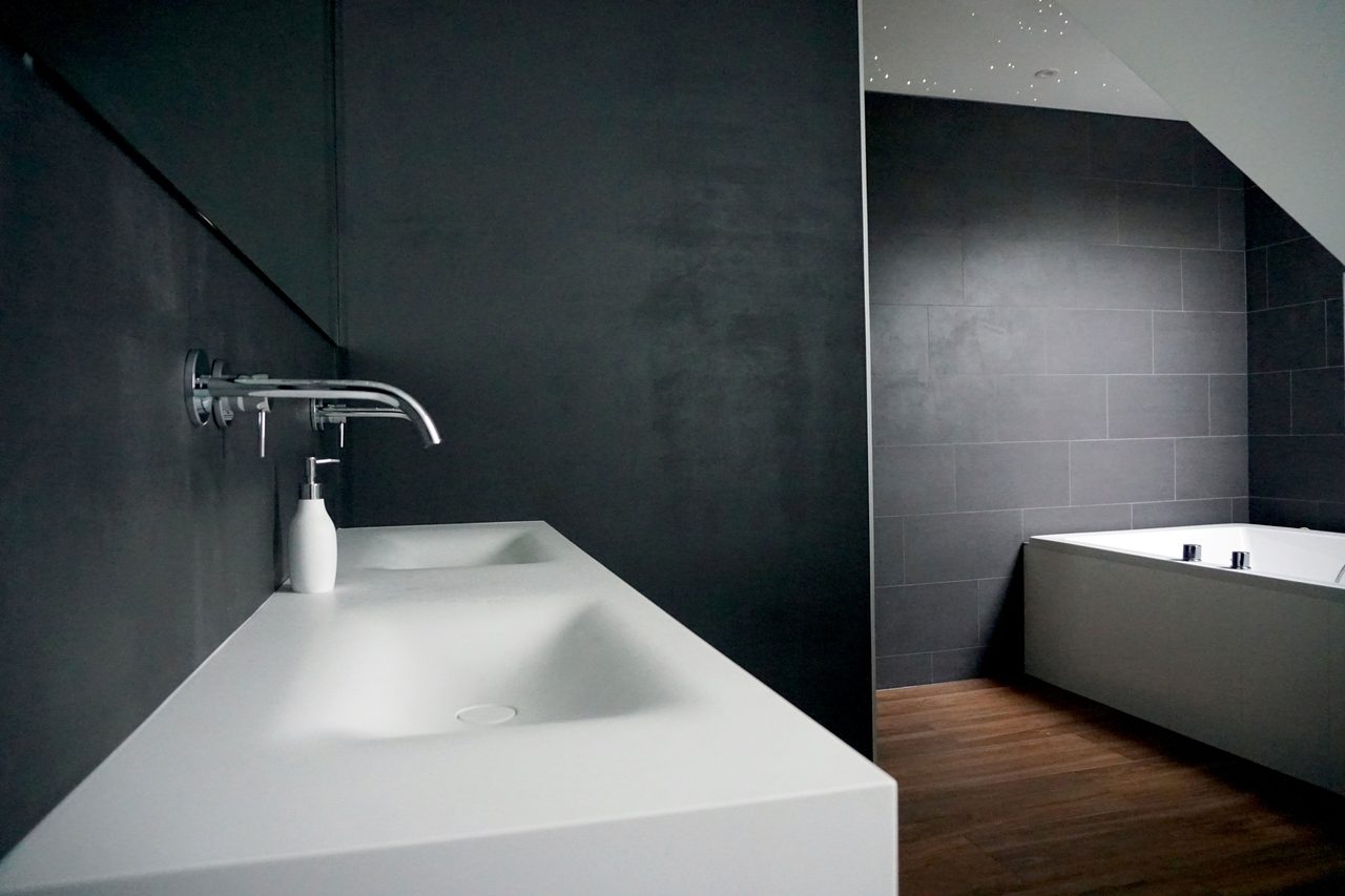 Badkamer met een donkere tegelwand en een wastafelblad van wit composiet