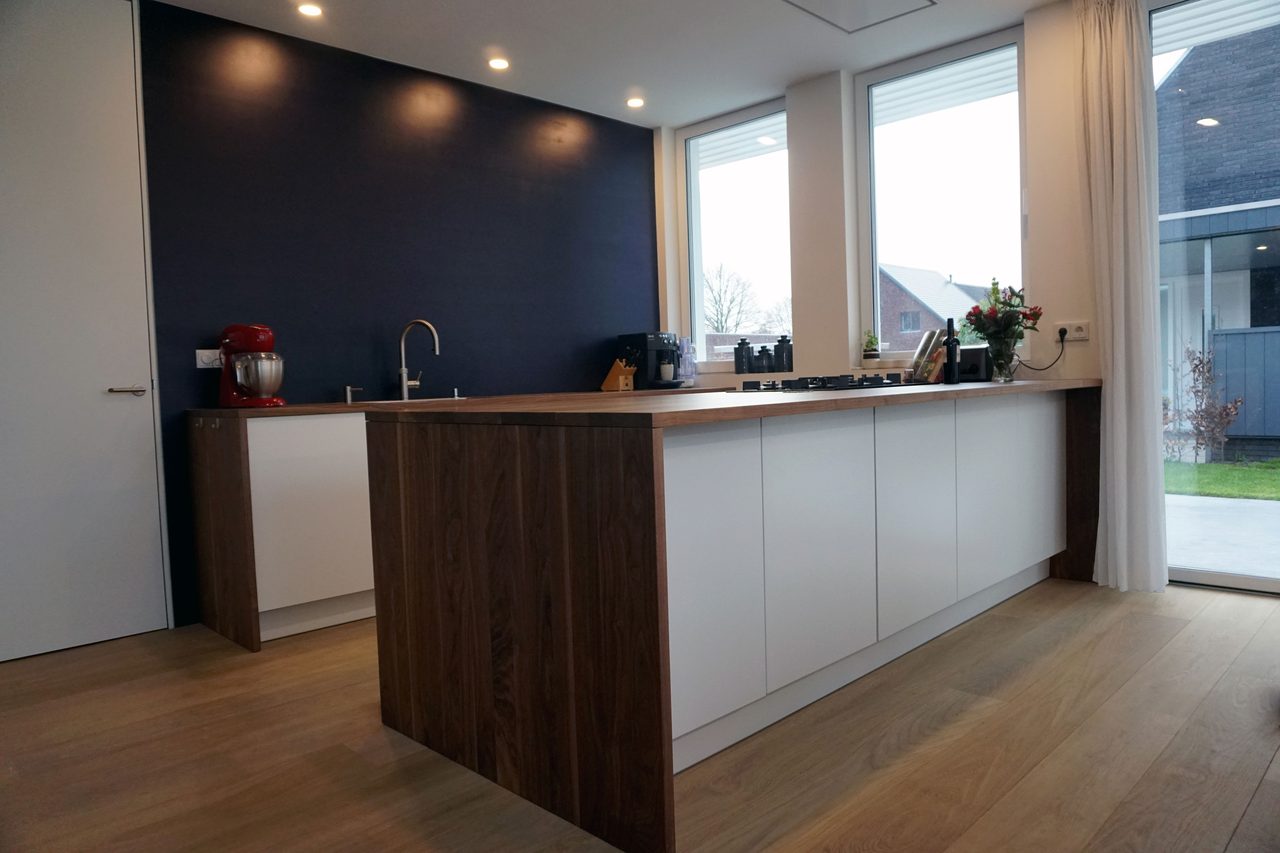 Keuken met donkere wand, notenhouten kastenwand en een wit kookeiland
