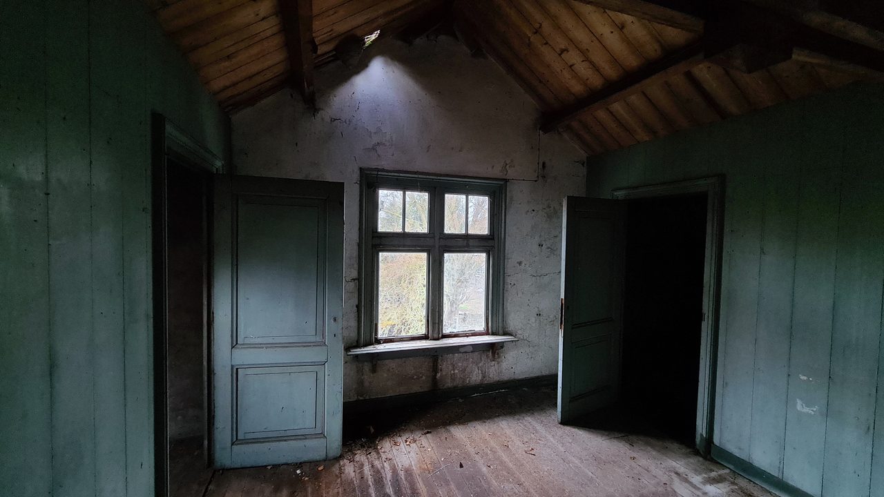 Zolderkamer met een houten schuine wand en groen geschilderde lambrisering, bestaande staat