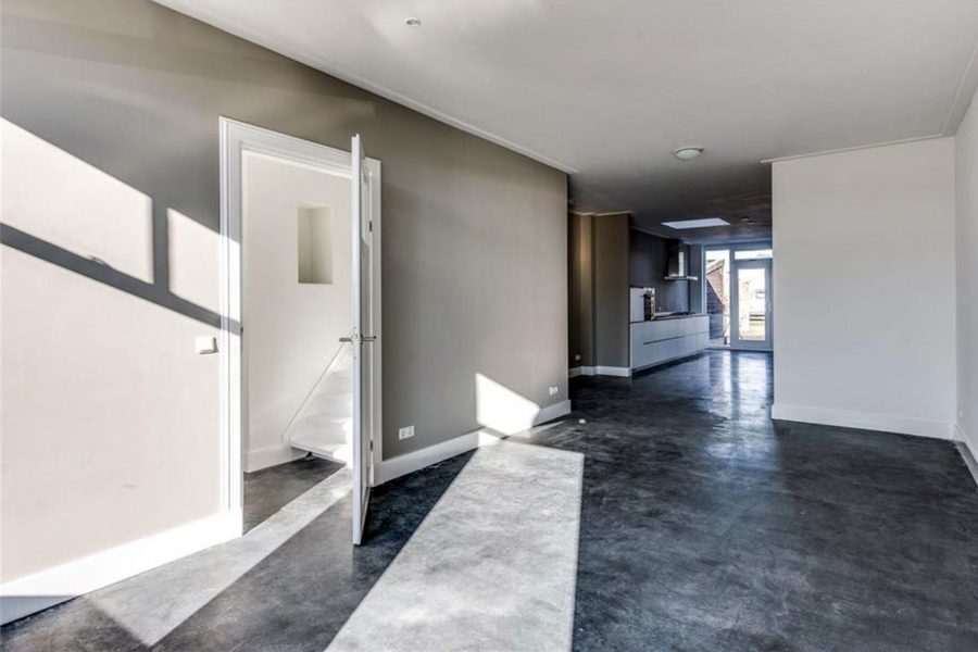 Hal met zicht door naar de keuken, met betonvloer en witte wanden