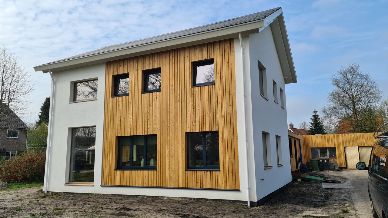 De gerenoveerde woning met wit stucwerk en verticale houten delen