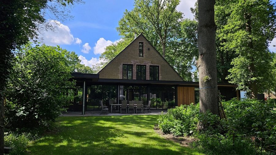 De woning gezien vanaf de achtertuin, tussen de bomen op het perceel